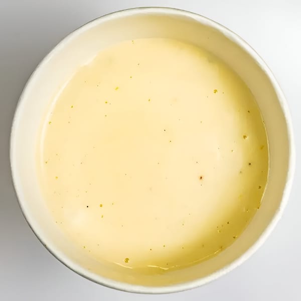 Creamy yellow sauce with specks of seasoning in a white paper cup.