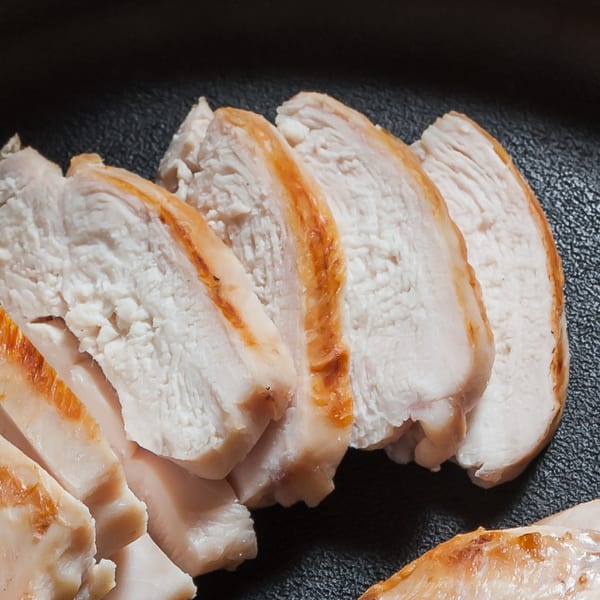 Close-up of several slices of cooked chicken breast with golden-brown edges on a dark surface.