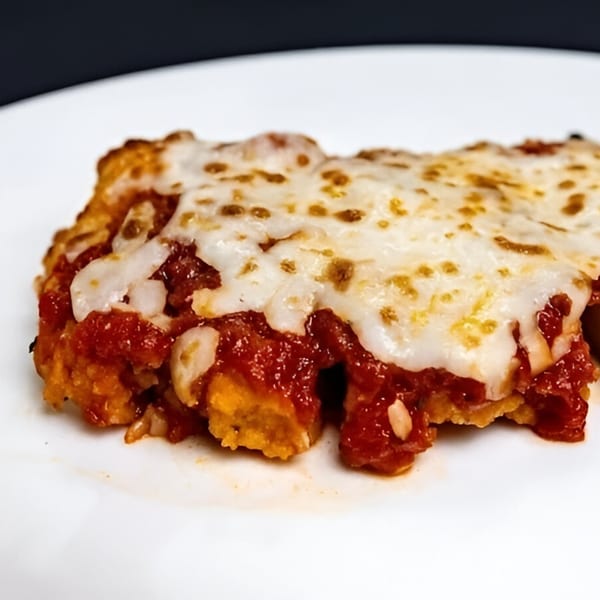 Close-up of a cheesy, saucy Italian dish with melted mozzarella on a white plate.