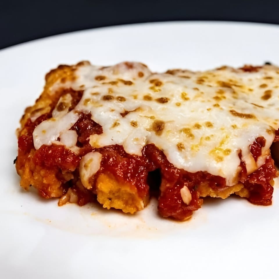 Close-up of a cheesy, saucy Italian dish with melted mozzarella on a white plate.