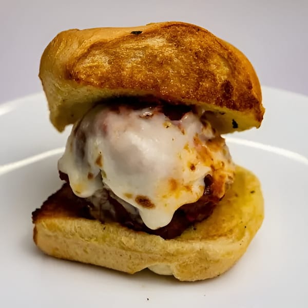 A By The Bucket meatball slider with melted mozzarella cheese on a toasted bun.