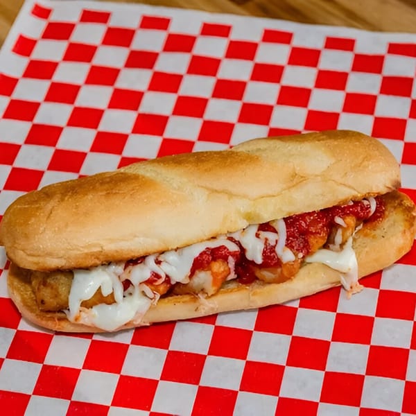 Meatball sub with melted mozzarella cheese and marinara sauce on a red and white checkered paper.