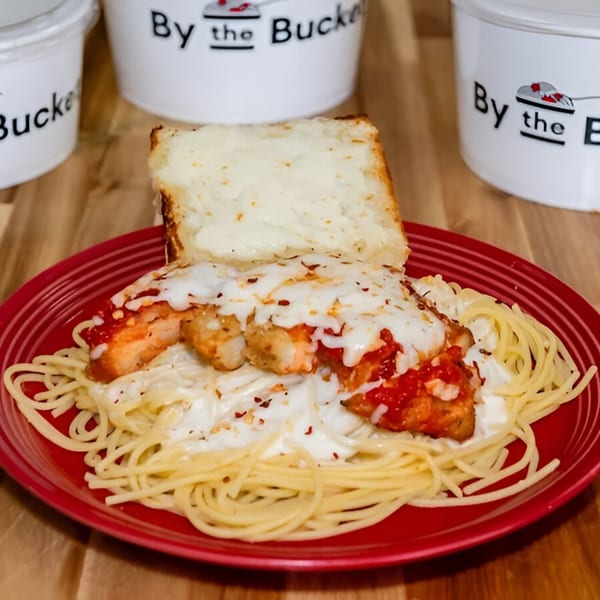 By The Bucket's chicken parmesan with spaghetti and garlic bread on a red plate.