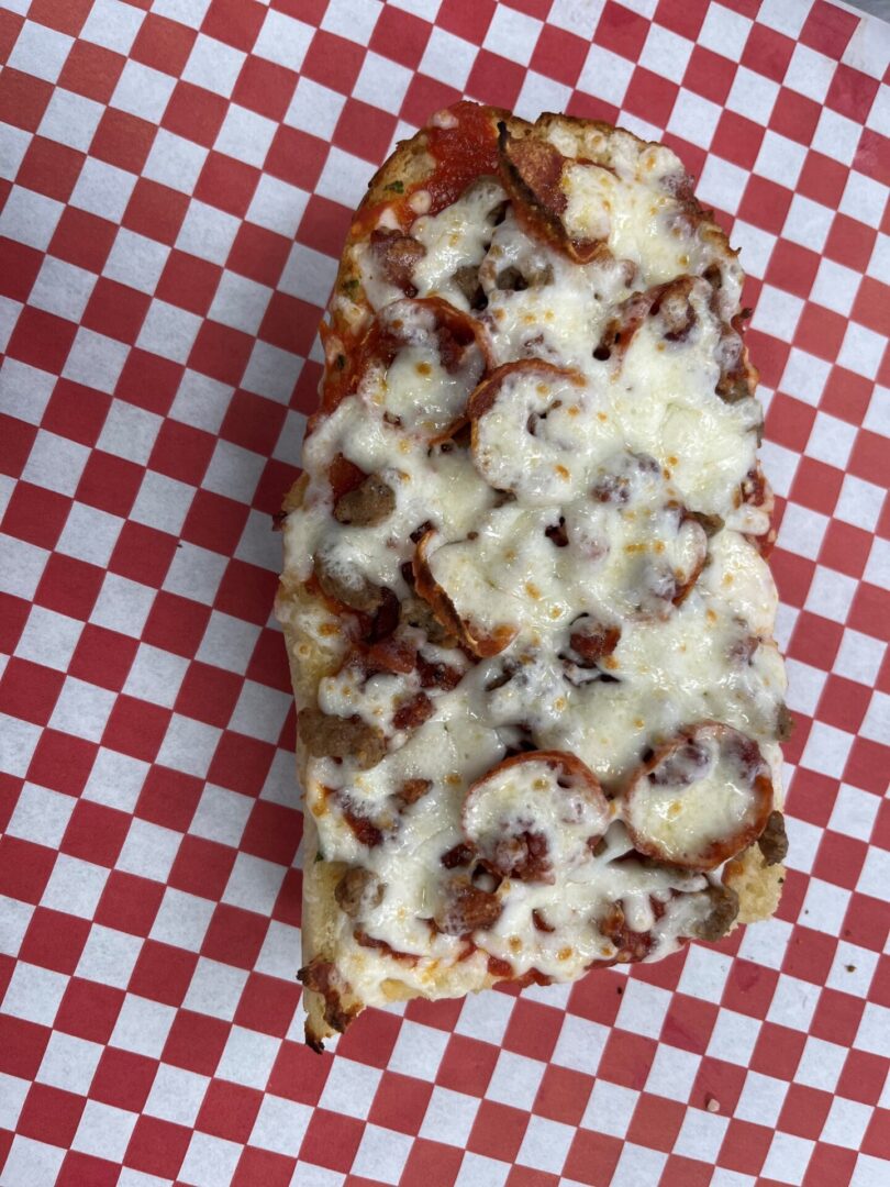 A piece of pizza sitting on top of a red and white checkered paper.